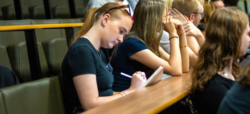 An apprentice sits in a lecture theatre, making notes as her peers listen to the presentation